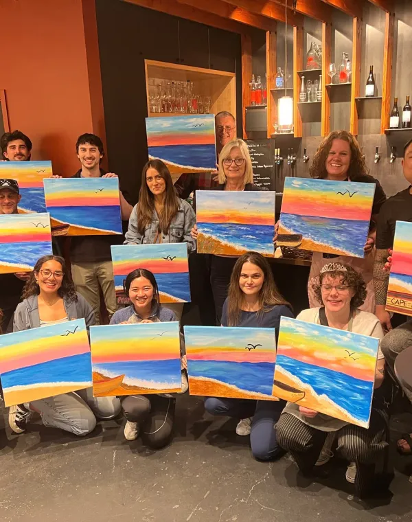 A paint night group holding their colorful finished landscape paintings