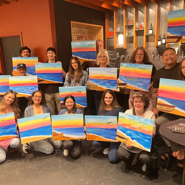 A paint night group showing their finished sunset landscapes