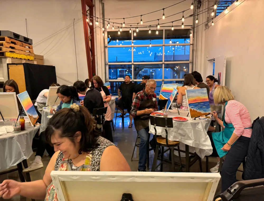 Paint party guests holding their finished sunset landscape paintings